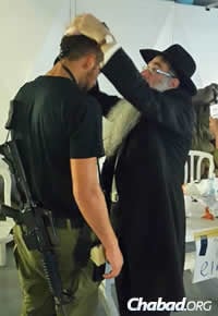 Rabbi Menashe Perman, director of Chabad of Chile, helps a soldier don tefillin. (Photo: CTVP)