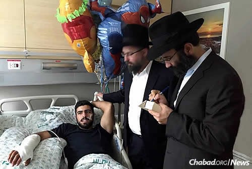 Chein, right, writes messages of love and hope in the Chitat book (Chumash, Tehillim and Tanya) given to a wounded soldier. His hand was severely injured, prohibiting his return to serve his country.