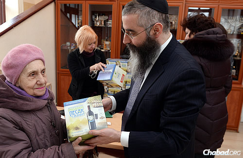 Rabbi Avraham Wolff, chief rabbi and head Chabad emissary in Odessa, the fourth-largest city in Ukraine, hands a box of shmurah matzah to Jewish woman. (FJC Photo)