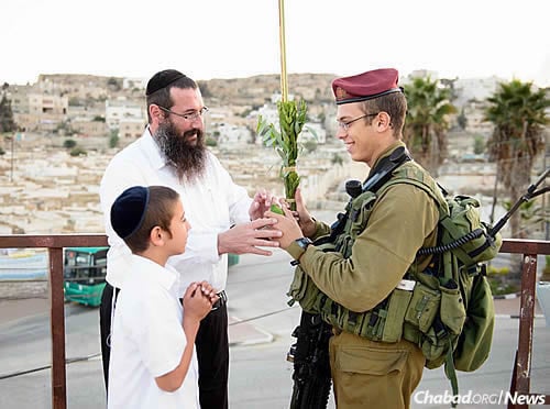 Rabbi Danny Cohen of Chabad of Hebron and his son Shneor offer the lulav and etrog to a soldier during Sukkot. (Photo: Israel Bardugo)
